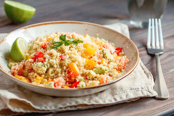 Couscous salad with fresh red and yellow bell peppers, avocado, tomatoes and lime. The concept of vegetarian and healthy food.