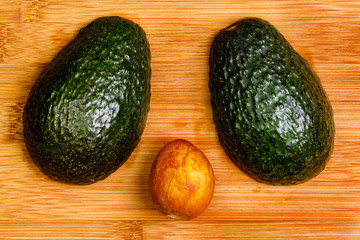 Two halves of an avocado face down on a bamboo cutting board with the pit on the surface between them.