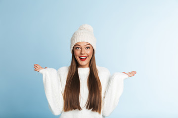 Cute amazing young woman wearing winter hat posing isolated over blue wall background showing...