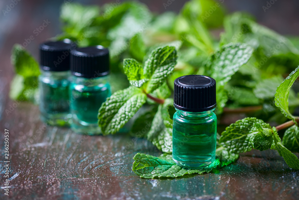 Wall mural Essential oil of peppermint in small bottles, fresh green mint on wooden background