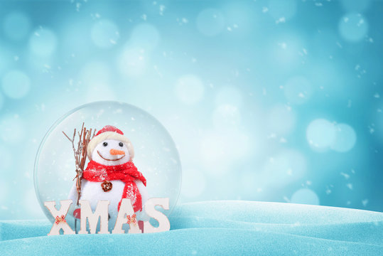 Snowman in New Year magic glass ball. XMAS letters beside. Free space on right side fot text. Bokeh in background.