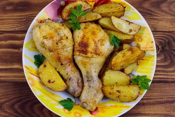 Baked chicken drumsticks with potatoes in a plate on wooden table