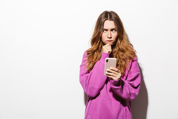 Portrait of resentful woman 20s wearing sweatshirt holding mobile phone while standing, isolated over white background