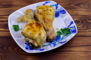 Baked chicken drumsticks with potatoes in a plate on wooden table