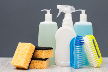 Bottles of dishwashing liquid, brushes and sponges on gray background.
