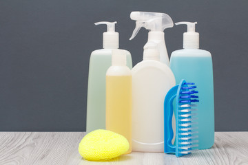 Bottles of dishwashing liquid, brush and sponge on gray background.