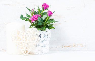 Decorative heart, pink roses and candles on white wooden backgro