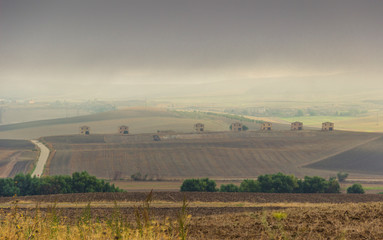 Fototapeta na wymiar Between Apulia and Basilicata: hilly rural landscape with farmhouses on plowed land dominated by clouds, Italy. Country road through plowed field.