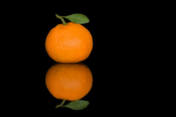 Fresh tangerine with a small leaf on a black background. Juicy ripe citrus on the glass with a clear and bright reflection.