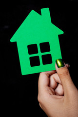 hand holding a little green paper house - black background