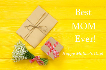 Happy Mother's day text on yellow rustic wooden background. greeting card and gift box concept spring flowers flat lay
