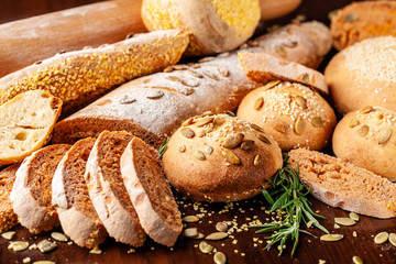 Homemade wholemeal tomato bread with basil and pumpkin seeds, baguette, buns, lie on a wooden table. Background image
