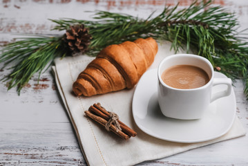 Cup of coffee and a croissant on Breakfast table. The concept of a winter Christmas greeting card