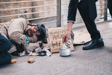 Businessman giving donation dollar cash with sleeping homeless person - obrazy, fototapety, plakaty