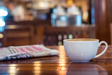 Hot espresso coffee cup with newspaper on wooden table lighting bokeh blur background