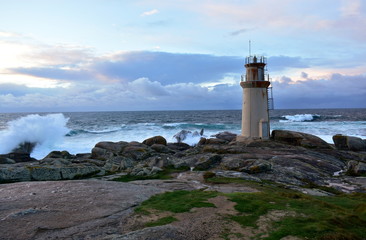Lighthouse with waves splashing against the rocks. Rainy day, sunset, blue and red sky with clouds. Muxia, Galicia, Spain.
