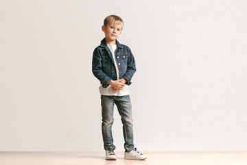 The portrait of cute little kid boy in stylish jeans clothes looking at camera against white studio wall. Kids fashion concept - Powered by Adobe