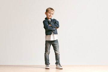 The portrait of cute little kid boy in stylish jeans clothes looking at camera against white studio...