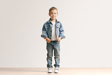 The portrait of cute little kid boy in stylish jeans clothes looking at camera against white studio...
