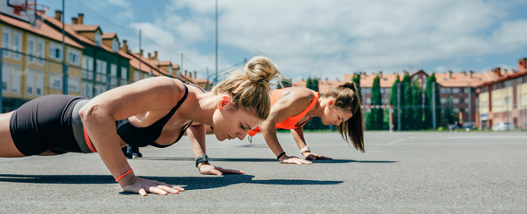 Two young sportswomen doing push-ups on a sports field
