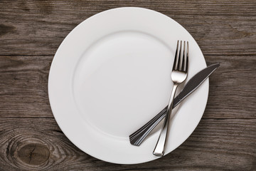 Empty white ceramic plate and cutlery on wooden table, top view