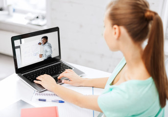 e-learning, education and technology concept - female student watching webinar on laptop computer at home office