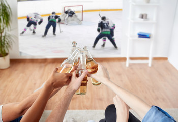 sport, entertainment and people concept - happy friends clinking beer bottles and watching ice...