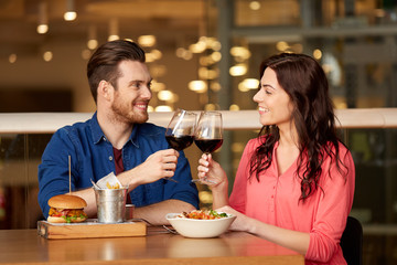 celebration, leisure and holidays concept - happy young couple eating and clinking glasses of red wine at restaurant