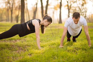 Young athletic couple doing push up outdoors. Athletic family engaged in sports on nature. Sport life.