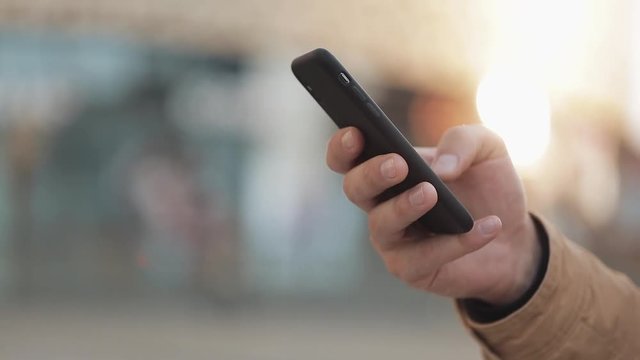 Hands of young man using smartphone in the street near shopping mall. Communication, online shopping, chat, social networking concept. Close up