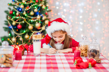 Fototapeta na wymiar Little girl in red christmas hat writes letter to Santa Claus