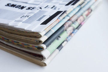 Pile of fresh morning newspapers on the table at office. Latest financial and business news in daily paper. Pages with information (headlines, articles, photos, text). Folded and stacked journals   