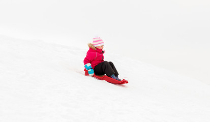 Fototapeta na wymiar childhood, sledging and season concept - happy little girl sliding down on sled outdoors in winter