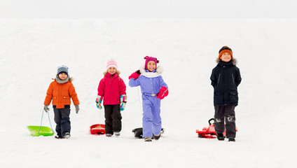 childhood, sledging and season concept - group of happy little kids with sleds in winter