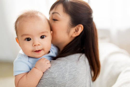 family and motherhood concept - close up of happy young asian mother kissing little baby son at home