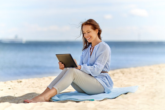 technology, people and leisure concept - happy smiling woman with tablet pc computer on summer beach
