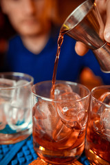 A red cocktail being poured from a shaker into a glass on a napkin on a bar top