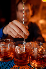 A red cocktail being poured from a shaker into a glass on a napkin on a bar top