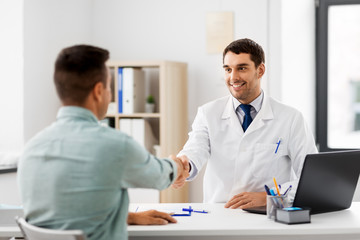 medicine, healthcare and people concept - smiling doctor and male patient shaking hands at hospital