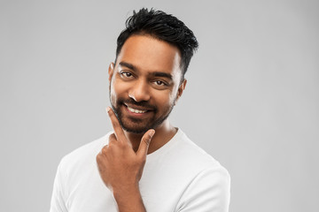 grooming and people concept - smiling indian man touching his beard over gray background