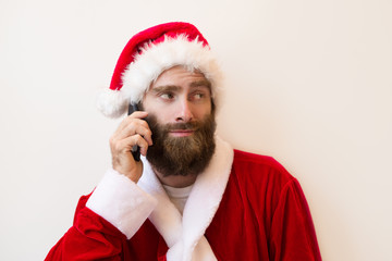 Bearded man wearing Santa costume and calling on phone. Handsome guy looking away. Christmas and communication concept. Isolated front view on white background.