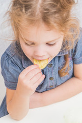 the girl, baby eat potato chips, not healthy food, on white brick wall background