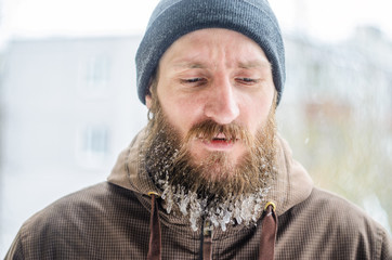 Young man with a beard covered with icicles and frozen droplets on the street after exercise. The...