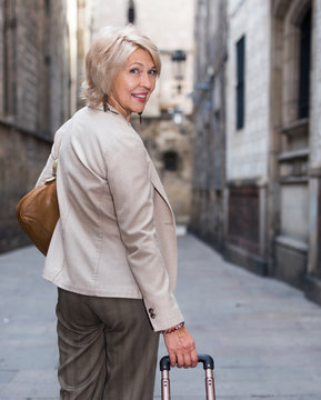 Elegant mature woman is posing with suitcase in time walking