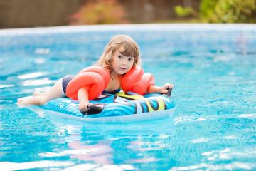 Adorable little girl with inflatable over-sleeves floats swiming in the pool, lying at the