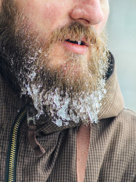 Part of the face of a serious and worried man is an icy beard with hanging icicles. Frosty harsh winter concept