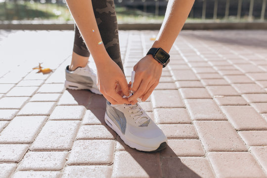 Closeup image of an athlete female tying up her laces on a bench at the park. She's bent down and wearing sport coach on her hand. Smart watch aside