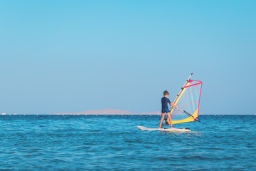 One child learning to windsurf in the open sea waters at beautiful sunset light, close up, windsurfing passtime and school with copy space