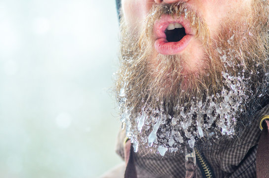 Young man with a beard covered with icicles and frozen droplets on the street after exercise. Evaporation from the mouth in winter