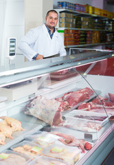 Adult salesman near display with cooled meat